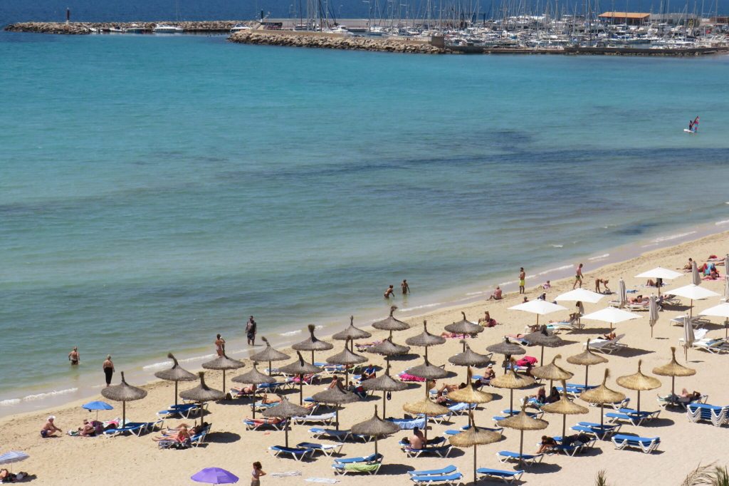 Aerial view of lounge chairs and bathers on a beach in front of a blue sea.