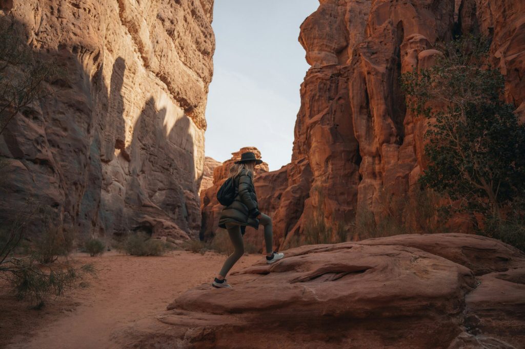 A woman in a hat is walking through a canyon.