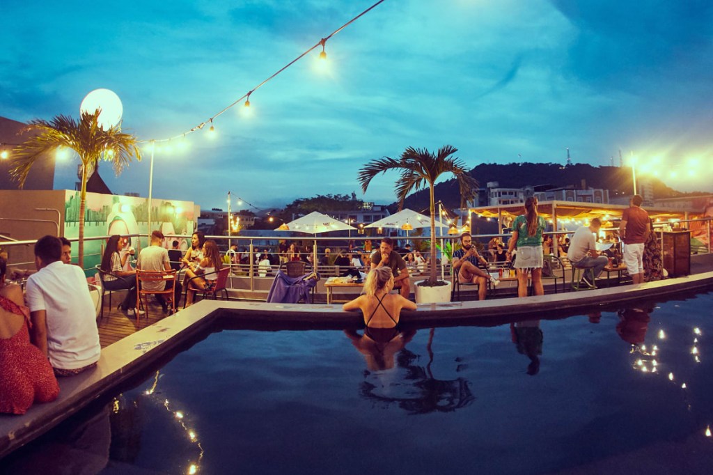 a pool and hostel rooftop with many young people flirting