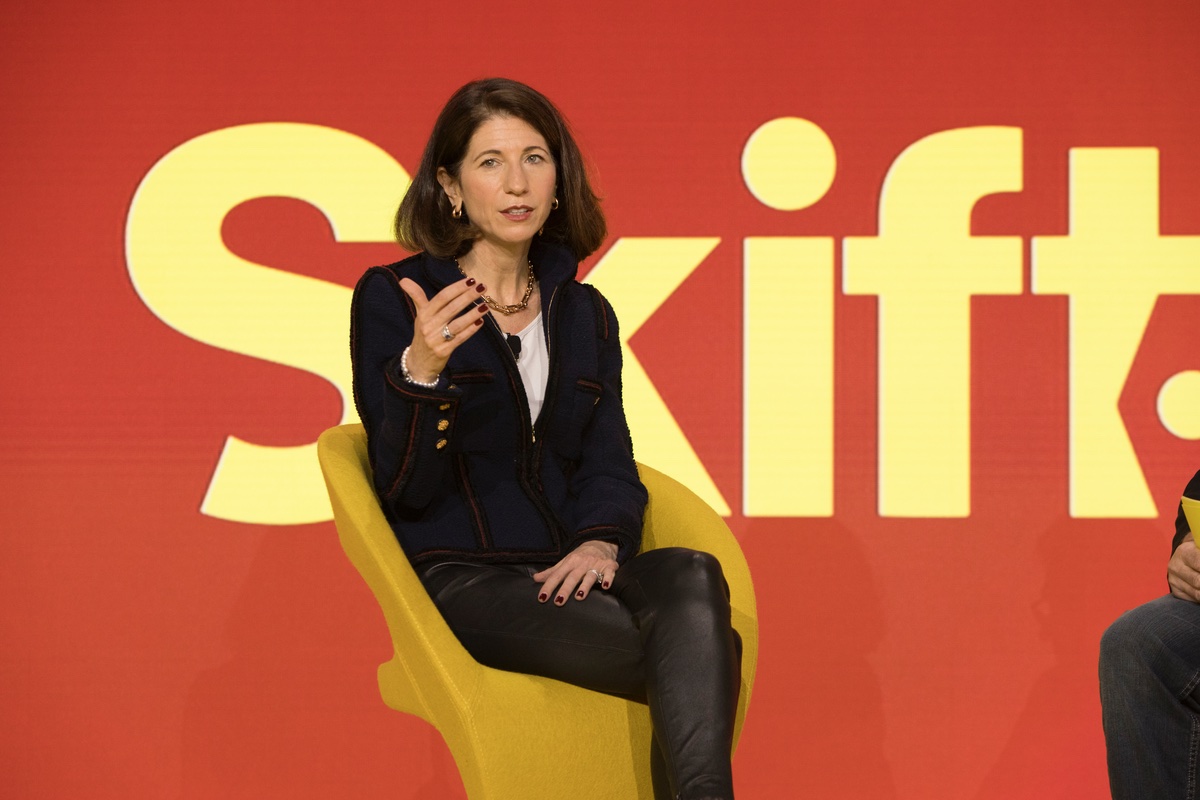 A woman seated on stage in front of a red background.