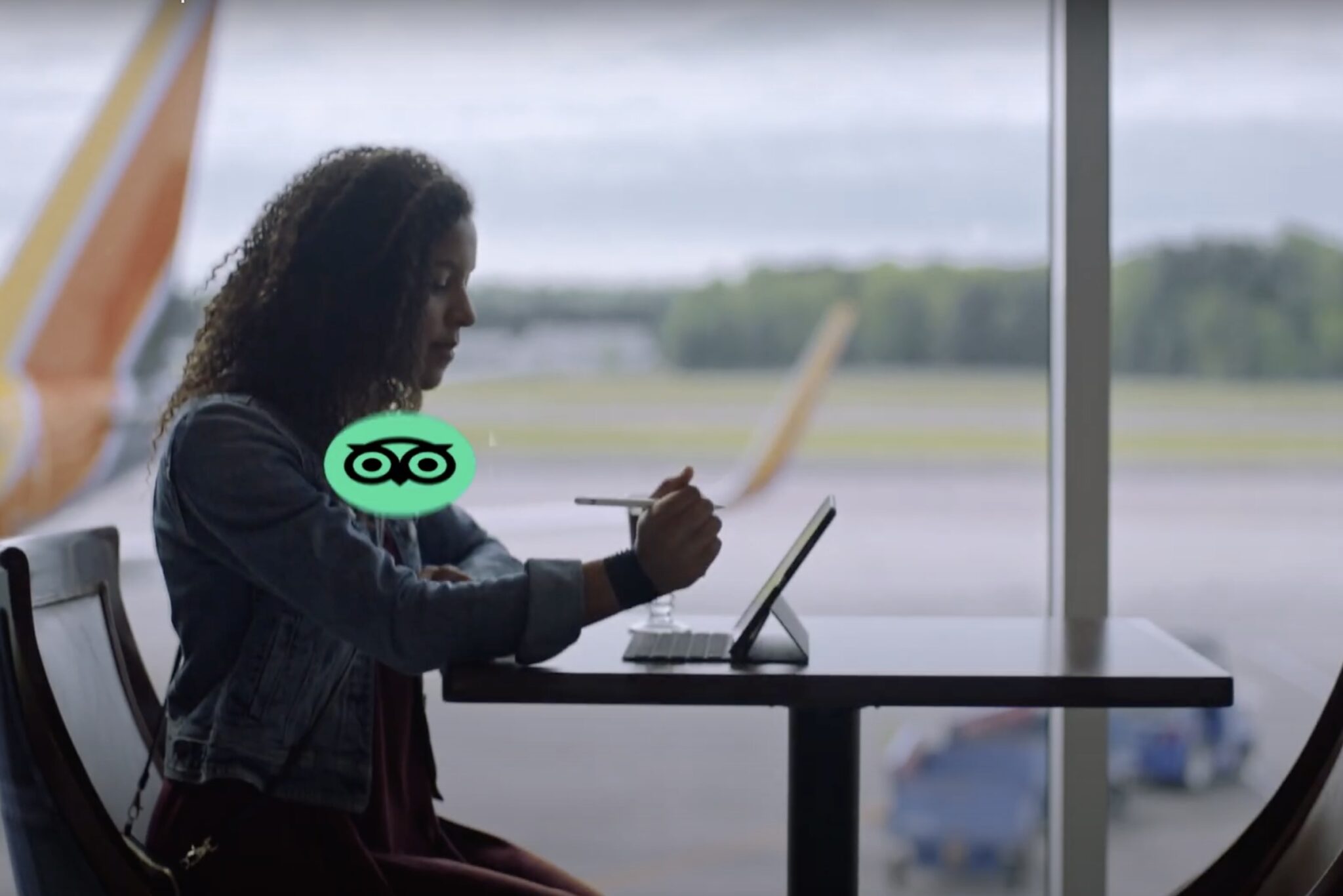 A women sitting at a table at an airport window. A plane is visible outside on the tarmac.