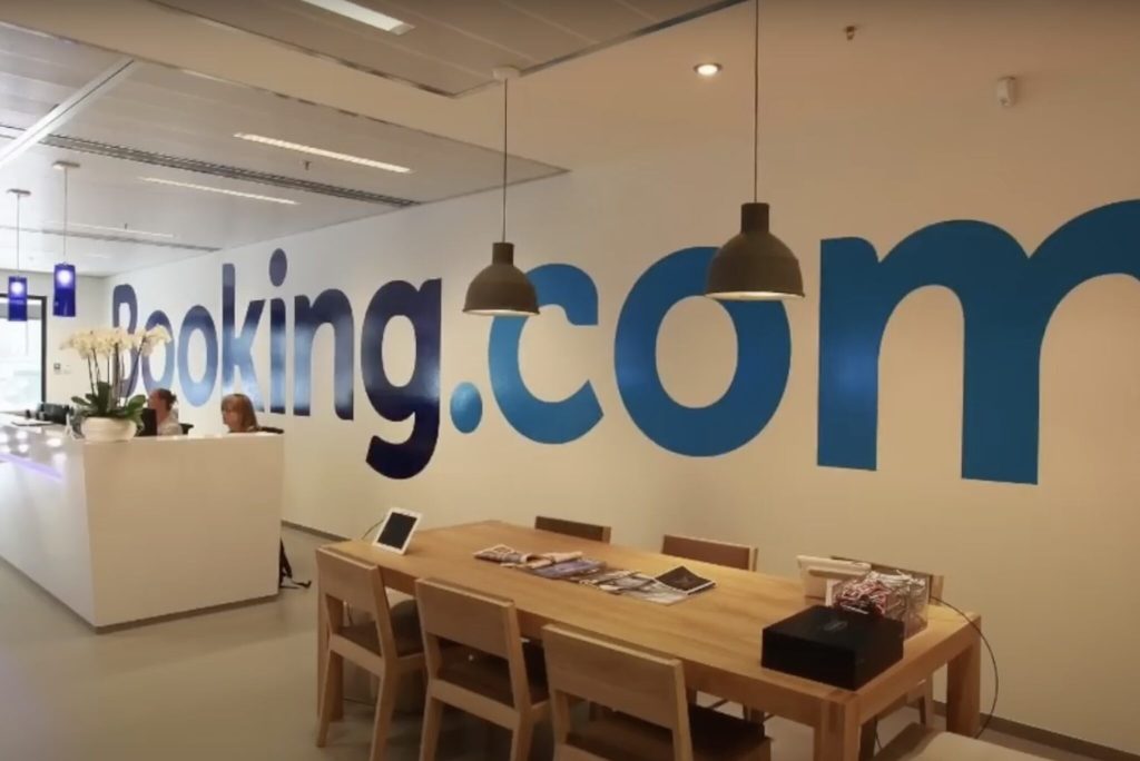 A sign with the Booking.com logo with a long desk in the foreground.