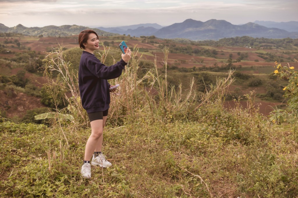 A female asian hiker takes a selfie with the surrounding mountai on a clear day