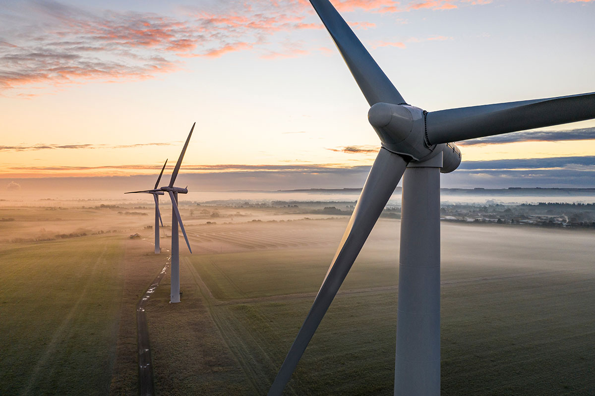 Aerial view of three wind turbines in the early morning fog at sunrise in the English countryside.