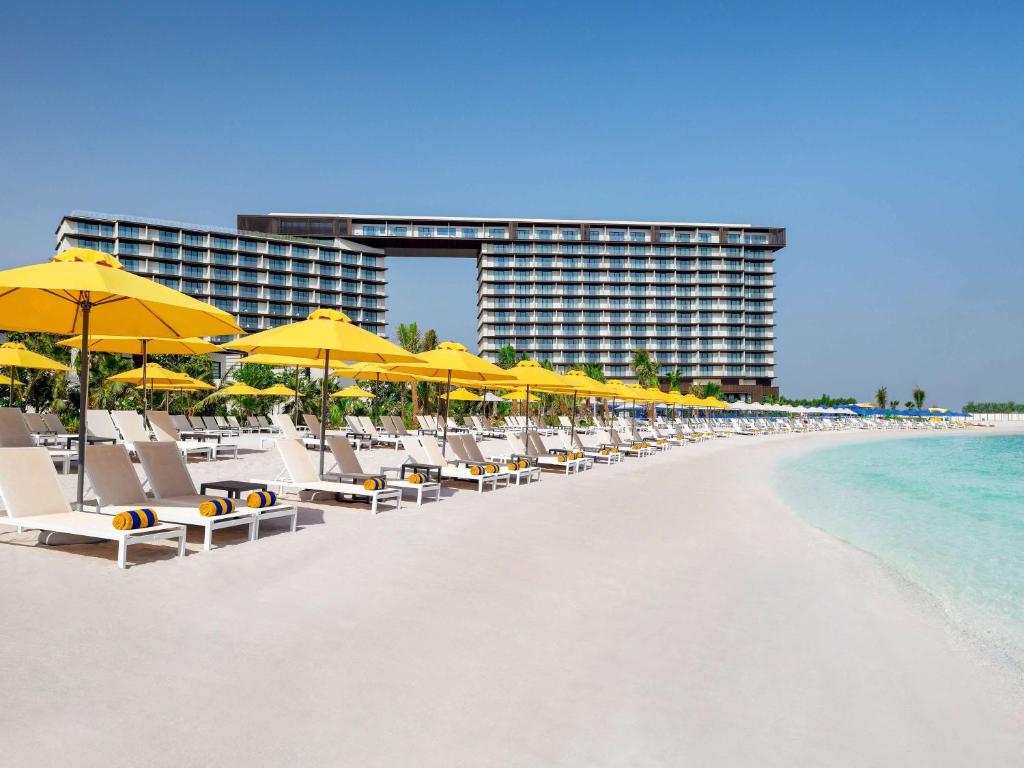 A white beach with loungers and umbrellas with a hotel in the background.