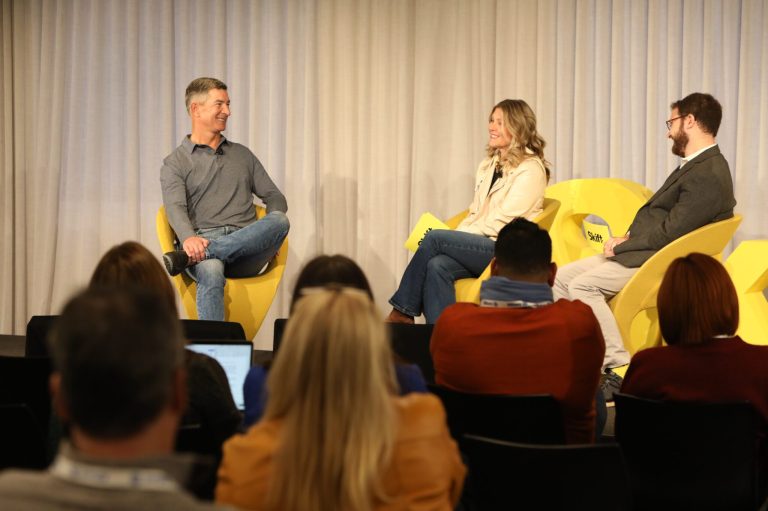 Three people sit on a stage at a Skift conference.