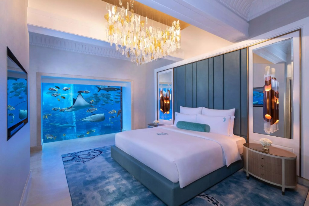 a large bed in a luxury hotel room with a window looking out to an aquatic scene.