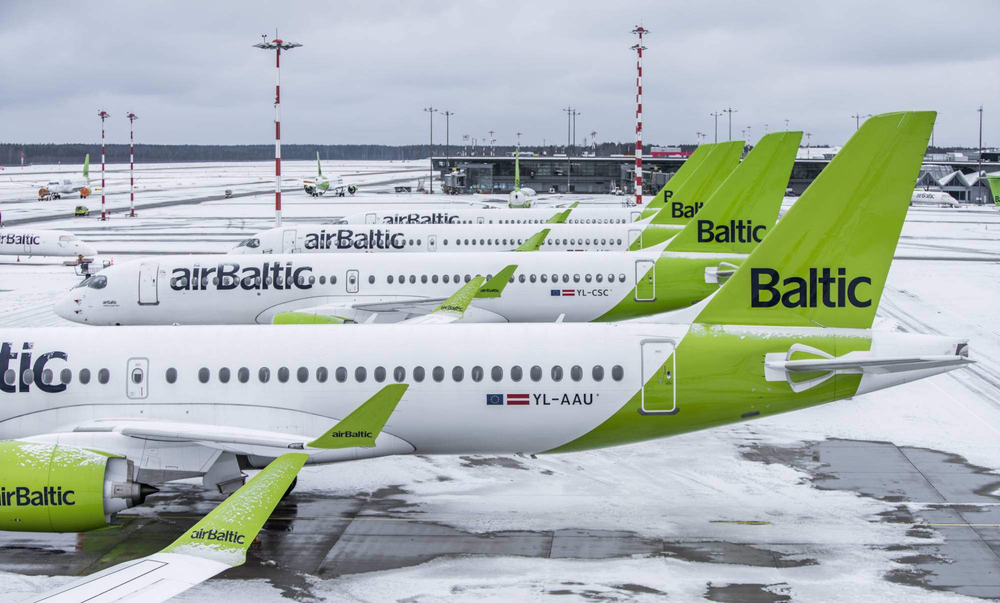 AirBaltic Airbus A220 planes are parked at a snowy airport.