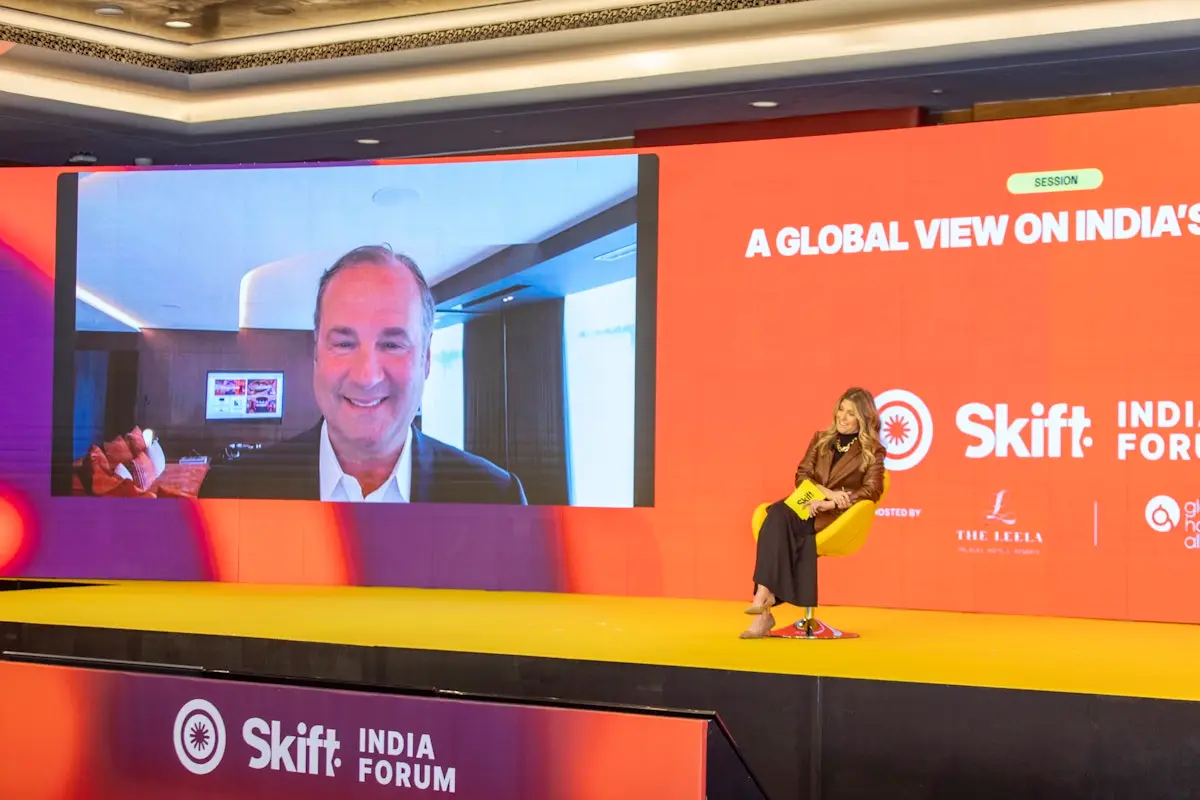 A woman sitting on a stage interviewing a man on a remote feed