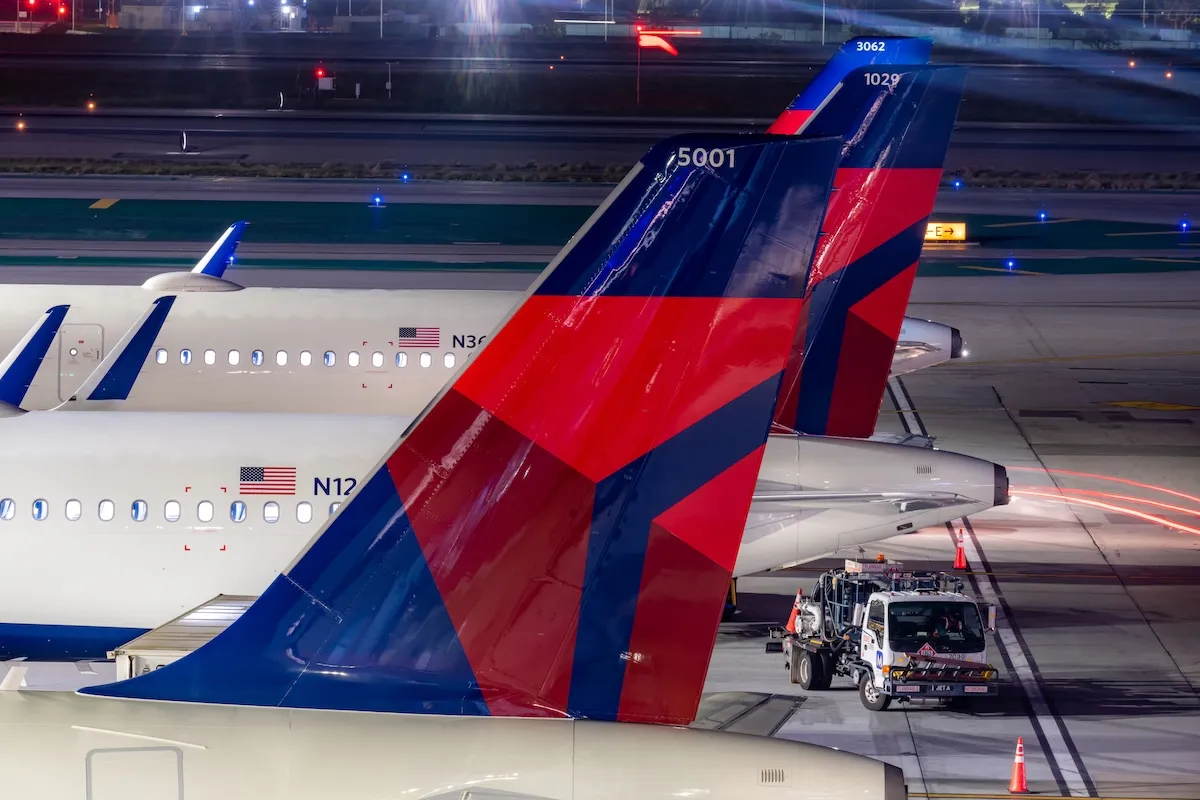 Tail wings of Delta planes on the tarmac at night.