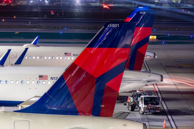 Tail wings of Delta planes on the tarmac at night.