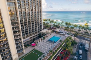 Image of a married hotel overlooking Waikiki Beach, seen from an aerial view of the hotel's pool, then the beautiful palm trees and ocean