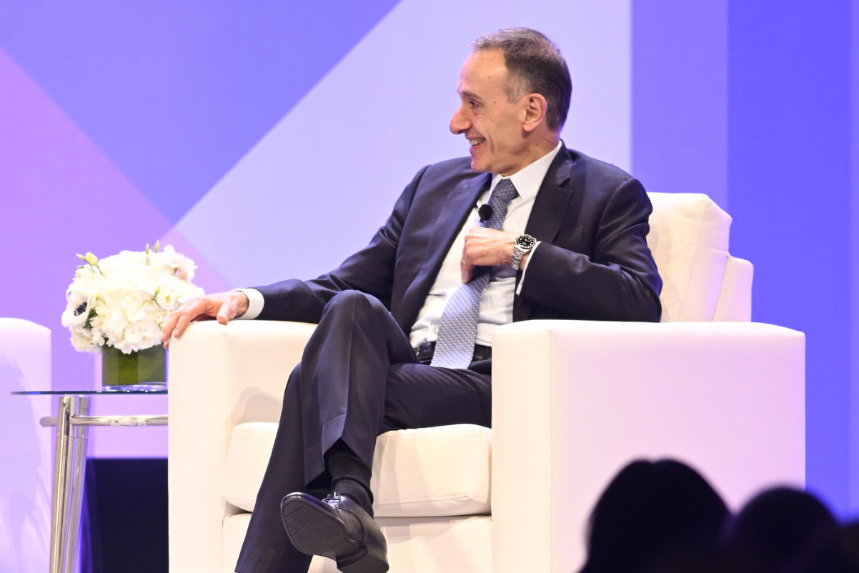 IHG CEO Elie Maalouf sitting in a white chair while wearing a suit and talking on-stage