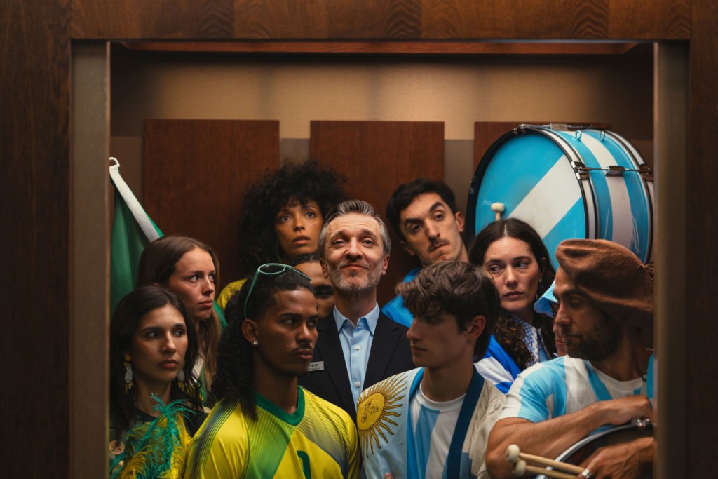 Image of football fans for Scotland's national team and Brazil's national team stuck in an elevator wearing their costumes or outfits, with a Marriott employee in the middle.